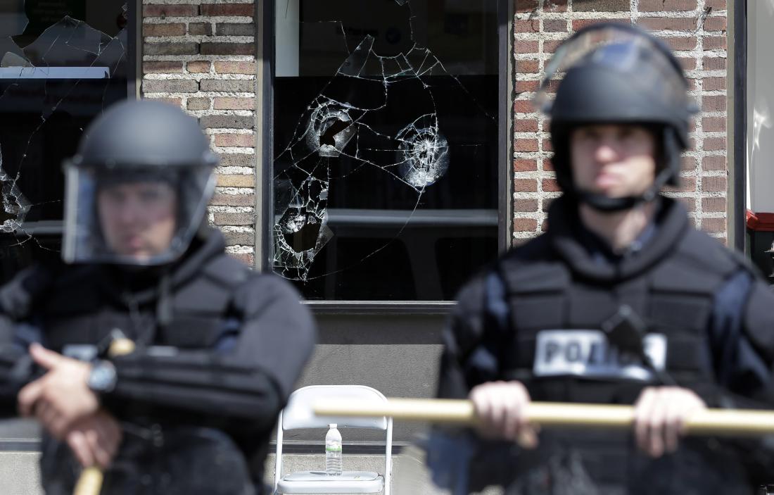 Broken store windows remain as members of the Anne Arundel County Police guard the intersection of North Avenue and Pennsylvania Avenue, Wednesday, April 29, 2015, in Baltimore. Schools reopened across the city and tensions seemed to ease Wednesday after Baltimore made it through the first night of its curfew without the widespread violence many had feared. People in Baltimore have been angry over the police-custody death of Freddie Gray.  (AP Photo/Patrick Semansky)