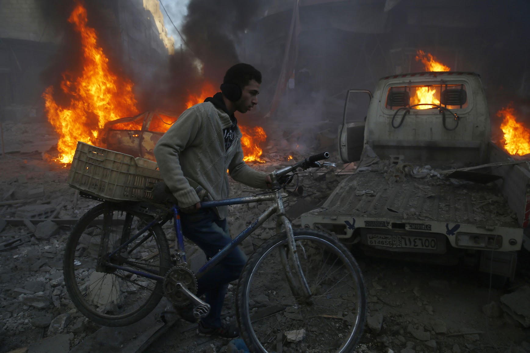 A man carries his bicycle past debris and burning cars following reported airstrikes in the town of Hamouria in the eastern Ghouta region, a rebel stronghold east of the Syrian capital Damascus, on December 9, 2015. The Syrian Observatory for Human Rights reported at least 11 civilians, including four children, were killed in strikes on the town of Hamouria, but said it was unclear if they were carried out by Russian or regime aircraft. AFP PHOTO / SAMEER AL-DOUMY